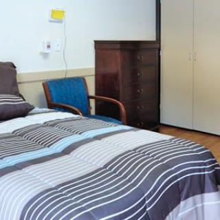 A cozy bedroom with patterned bedding, an armchair, and a wardrobe.