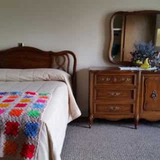 A cozy bedroom featuring a bed with a colorful quilt and a vintage dresser with a mirror.