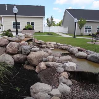 A beautifully landscaped backyard with a rock-lined pond and adjacent houses.