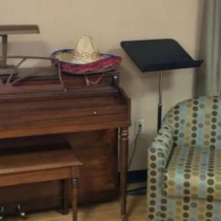 A cozy room with a piano and a music stand next to an upholstered chair.