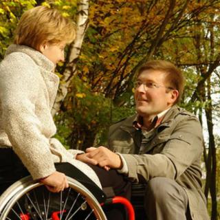 A person in a wheelchair and another individual engaging in a conversation in an autumn setting.