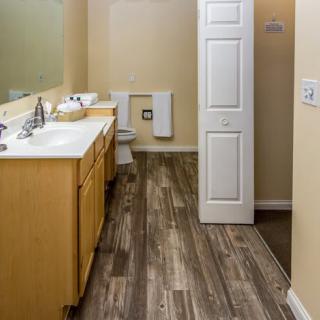 A modern bathroom with a wooden cabinet, a large mirror, and hardwood flooring.