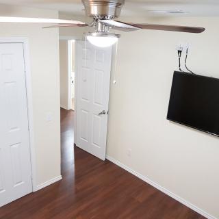 A room with a ceiling fan, wall-mounted TV, hardwood floors, and multiple doors.