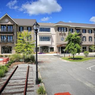 A modern building situated in an urban area, surrounded by greenery and featuring a pathway.
