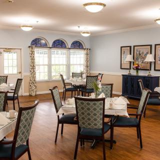 A cozy dining room with neatly arranged tables and chairs, featuring soft lighting and decorative elements.
