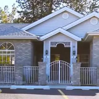 A brick residential house with a gable roof and white fencing.