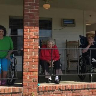 Elderly individuals in wheelchairs sitting on a porch of a brick building.