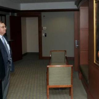 A man in a suit looks at a portrait painting in an office setting.