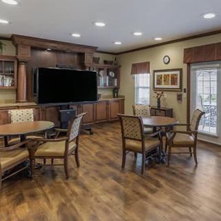 A cozy living room with tables, chairs, and a large television on a wooden floor.