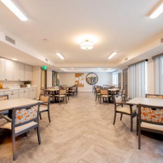 A modern dining room with neatly arranged tables and chairs, featuring bright lighting and a wooden floor.