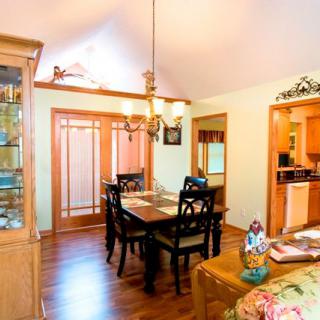 A cozy dining room with a wooden table and chairs, featuring a chandelier and a view into the kitchen.