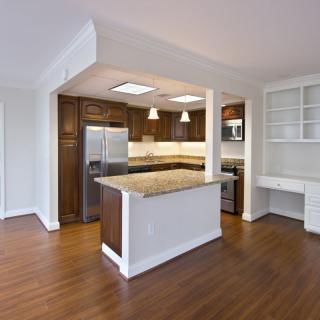 A modern kitchen featuring wooden flooring, a central island, and stainless steel appliances.