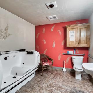 A bathroom featuring a walk-in bathtub, toilet, and sink, accented by red wallpaper and a wooden cabinet.