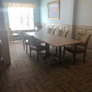 A well-lit conference room with a long table and surrounding chairs, featuring a window and carpeting.