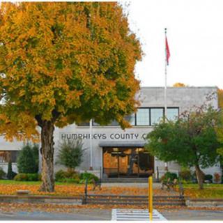 A county office building surrounded by autumn foliage with a flagpole at the entrance.