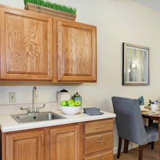 A cozy kitchen corner with wooden cabinets, a sink, and a dining area featuring a set table and comfortable chairs.