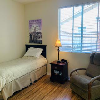 A cozy bedroom with a single bed, armchair, and a nightstand under a window.