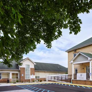 A residential-style building with a tree in the foreground and a parking lot.