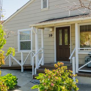A charming house with a small front porch surrounded by greenery on a sunny day.