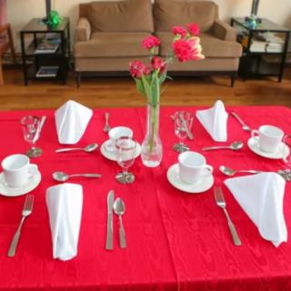 A beautifully set dining table with a red tablecloth and elegant place settings, featuring white napkins, tea cups, and a floral centerpiece.
