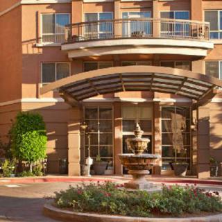 A modern building entrance with a glass canopy and a decorative fountain surrounded by plants.