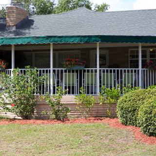 A house with a covered veranda and a well-maintained garden in the front yard.