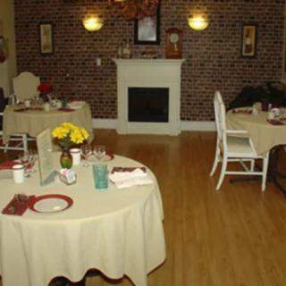 A cozy restaurant interior featuring a fireplace, round dining tables with tablecloths, and a brick wall.