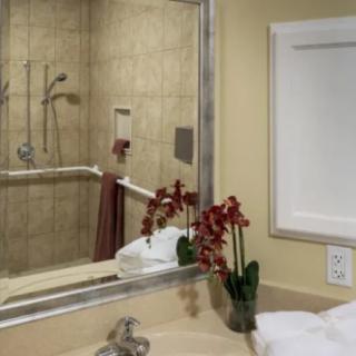 A bathroom featuring a mirror, sink, shower area, neatly folded towels, and decorative flowers.