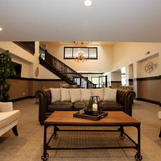 A spacious and elegantly designed living room with a central sofa, coffee table, and a staircase leading upstairs.