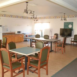 A community room with tables, chairs, a kitchenette, and a television.