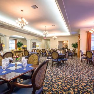 An elegant dining room with neatly set tables and chandeliers overhead.