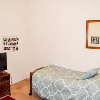 A minimalist bedroom with a single bed and a small television on a stand.
