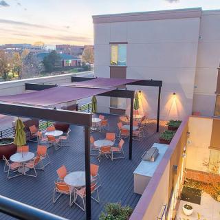 A rooftop patio with modern furniture, surrounded by an urban landscape at sunset.