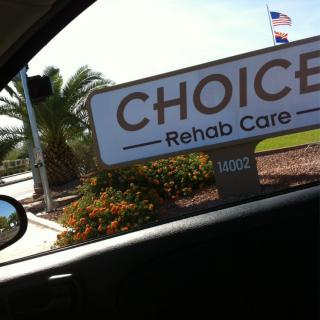 View from a car window of a sign for Choice Rehab Care with palm trees in the background.