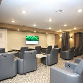 A modern theater room with comfortable recliner chairs facing a large television.