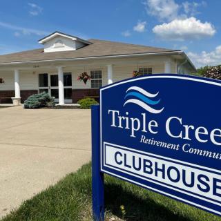 The clubhouse of Triple Creek Retirement Community with a prominent sign in front.