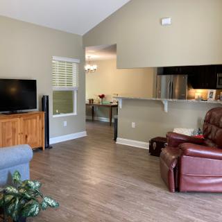 A cozy living room featuring a television, a comfortable sofa, and a recliner, with an open layout connecting to the kitchen.