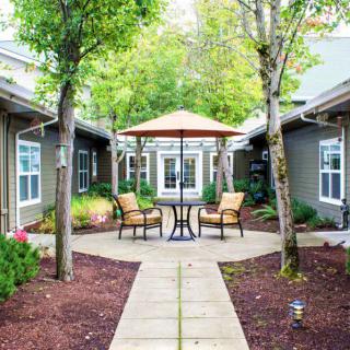 A serene courtyard with outdoor seating and a large umbrella, surrounded by trees and landscaped paths.
