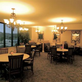 A well-lit dining room with several round tables and chairs, decorated with chandeliers and large windows.