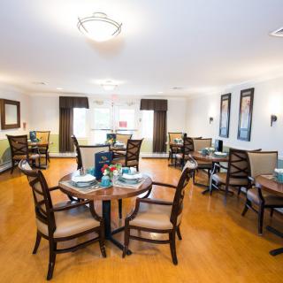 A spacious dining area with several round tables and chairs, featuring a well-lit interior and hardwood floors.