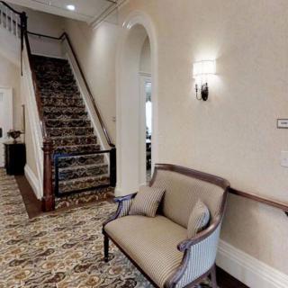 A cozy hallway featuring a staircase with decorative carpet, elegant lighting, and a comfortable seating area.