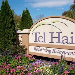 Entrance sign for Tel Hai, a retirement community, surrounded by colorful flowers and greenery.