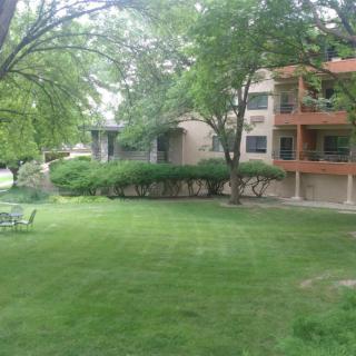 A serene view of an apartment building surrounded by a well-maintained lawn and trees.