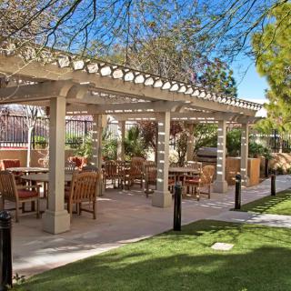 An outdoor seating area under a pergola, surrounded by a garden setting.