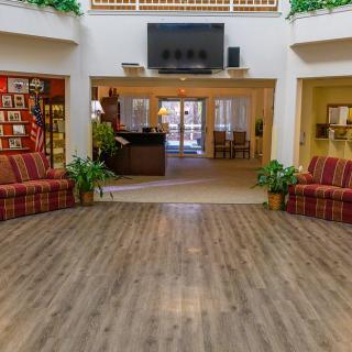 A spacious lobby with wooden flooring, featuring comfortable sofas and decorative plants.