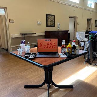 A conference room table set up with a laptop displaying 'Bravo' and various condiments, suggesting a casual meeting or presentation.