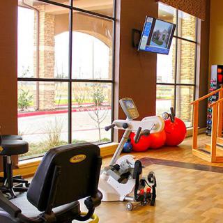 A well-lit gym with exercise equipment, including a stationary bike and fitness balls.