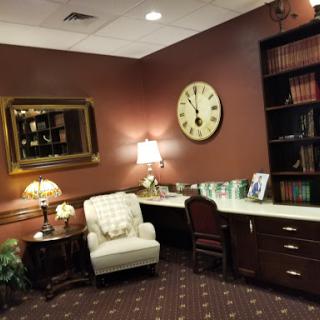 A cozy and inviting office waiting area featuring a bookshelf, comfortable chair, and a large clock on the wall.