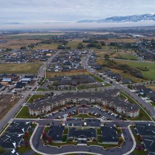 Aerial view of a suburban residential area with roads and houses, set against a backdrop of mountains under an overcast sky.