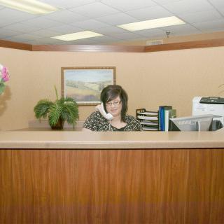A receptionist at an office desk talking on the phone, surrounded by plants and office supplies.